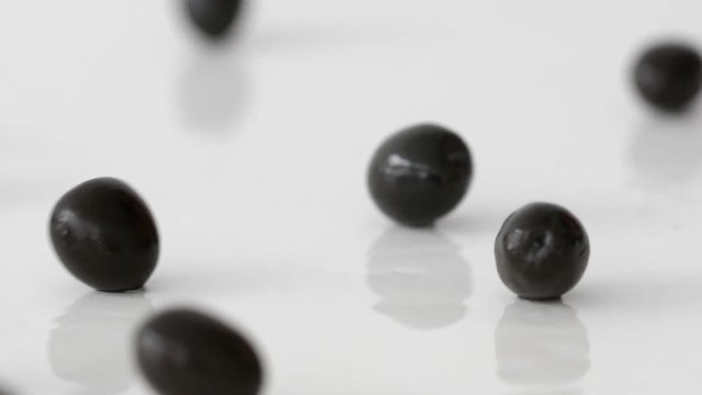 Isolated black olives roll on the table on a white background