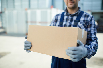 Close-up of moving company worker in gloves holding cardboard box and carrying it at container...