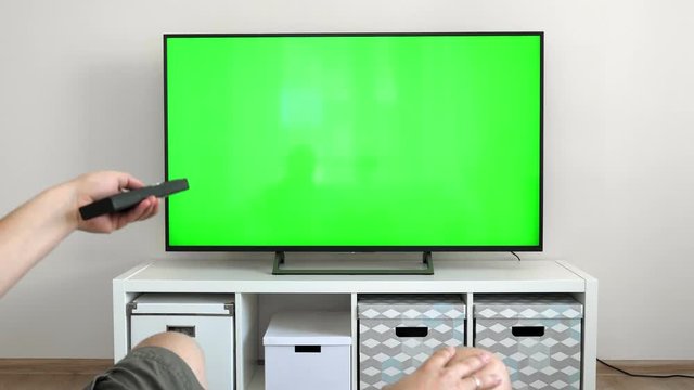 Watching tv with green screen at home interior. Push buttons on remote