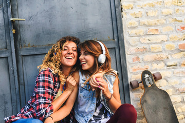 Skate girls sitting in the street hanging out listening music with earphones and smartphone