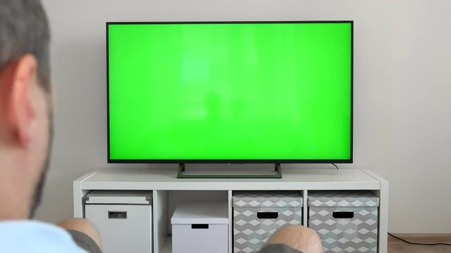 Watching tv with green screen at home interior. Push buttons on remote