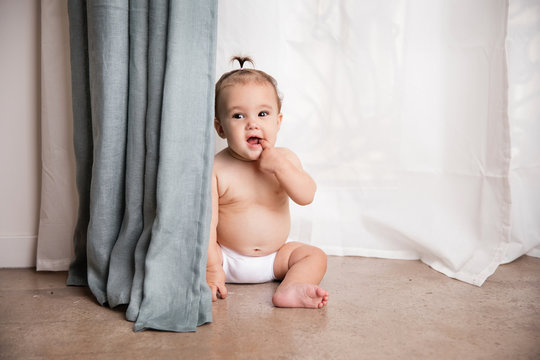 Cute baby girl sitting on floor behind curtains