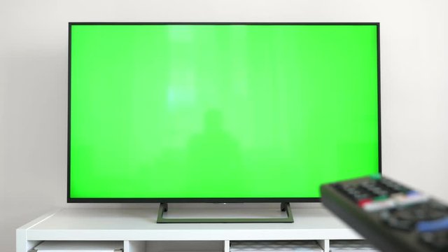 Watching tv with green screen at home interior. Push buttons on remote. Changing channels on television