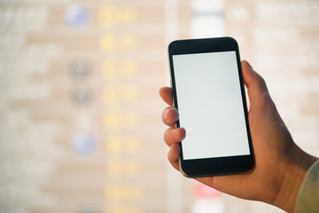 Mockup image of female hands holding black mobile phone with blank white screen over flight board in airport terminal