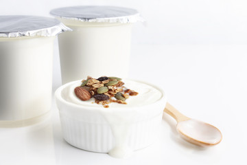 Healthy flavored yogurt in plastic cup and ceramic bowl with cereal and wooden spoon isolated on the white background. With copy space for your text.