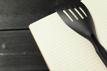 Blank sheet of opened notepad and kitchen utensils on  table with tablecloth, copy space
