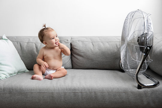 Baby girl sitting on sofa next to fan
