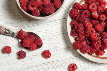 Ripe sweet raspberries in bowl, in cup and in saucer on wooden table.