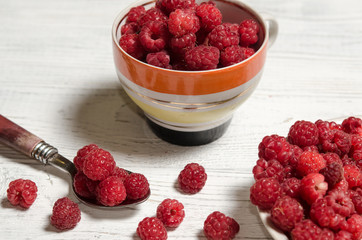 Ripe sweet raspberries in bowl, in cup and in saucer on wooden table.