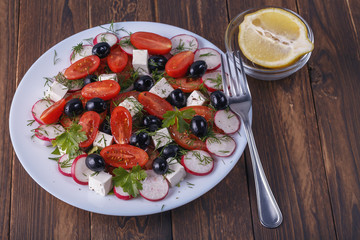 plate with salad with red tomato, radish, olives and cheese on a wooden table