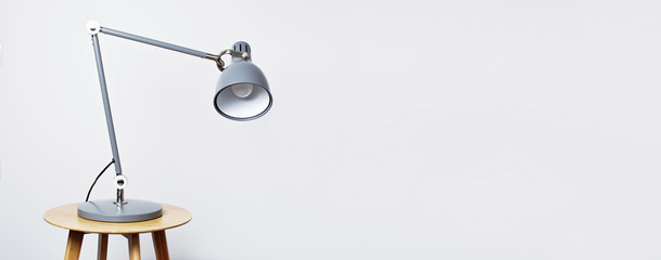 A gray table lamp in the interior against a white wall. The concept of business or education with a place for your text. Detail of interior, minimalism background.