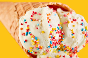 ice cream balls with colored sugar sprinkles in a Waffle Cone on a yellow Background. Vanilla ice cream in a waffle cone.