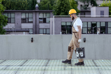 side view of builder in protective helmet and googles carrying bucket of cement at construction site © LIGHTFIELD STUDIOS