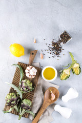 Fresh ripe green artichokes on cutting board ready to cook and ingredients garlic, lemon and olive oil