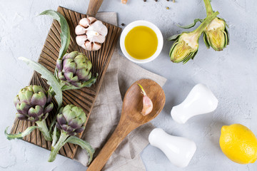 Fresh ripe green artichokes on cutting board ready to cook and ingredients garlic, lemon and olive oil