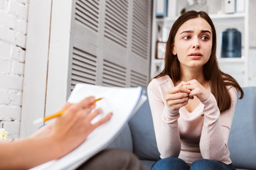 Health problems. Thoughtful young patient looking into the distance while sitting with her therapist and describing her illness