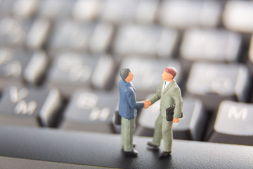 Business deal or agreement and success concept. Two miniature businessmen shaking hands while standing on the keys of a black keyboard.