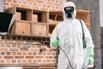 pest control worker in uniform standing with sprayer in kitchen