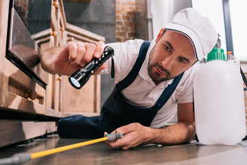 pest control worker lying on floor and spraying pesticides in kitchen - Powered by Adobe