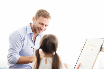 Obraz premium Young father teaching daughter to draw a picture. Happy time together. Setup studio shooting. Selective focus at father.