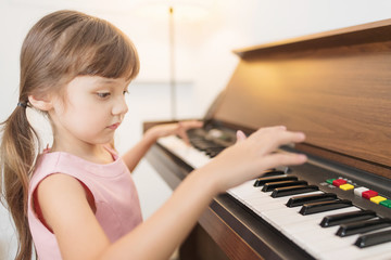 Adorable girl playing piano at home. Setup studio shooting.