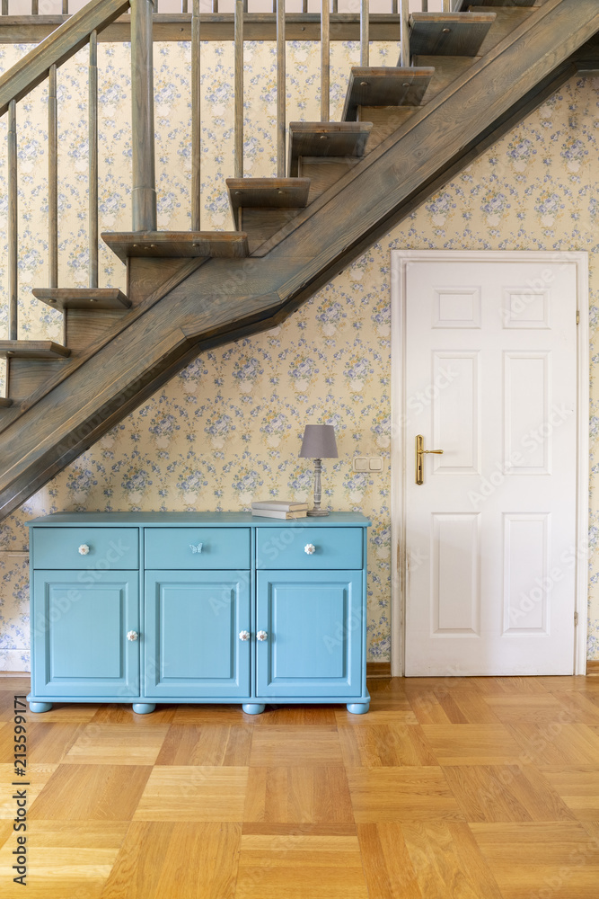 Wall mural Blue cabinet with lamp next to white door in hall of house with stairs and wooden floor. Real photo