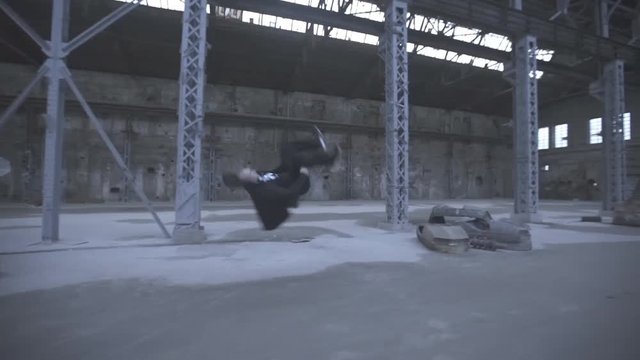 Male free runner jumping over car and doing parkour tricks in an abandoned building. Guy showing acrobatic stunts and somersaulting indoor. Concept of sportive lifestyle. Side view Closeup Slow motion