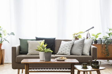Real photo of a sofa with cushions standing behind the tables in bright, vintage living room...