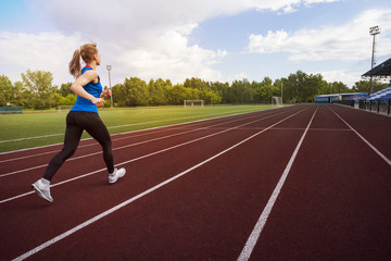 Athletic young sportswoman sprinting on running track stadium.