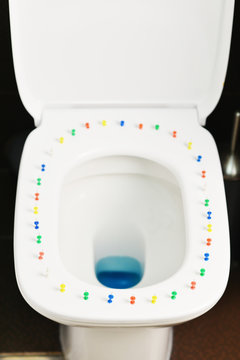 Conceptual image of a hemorrhoid disease with multi-colored thumbtacks on toilet bowl cover
