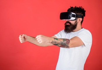 Virtual racing concept. Man with beard in VR glasses driving car, red background. Hipster on...