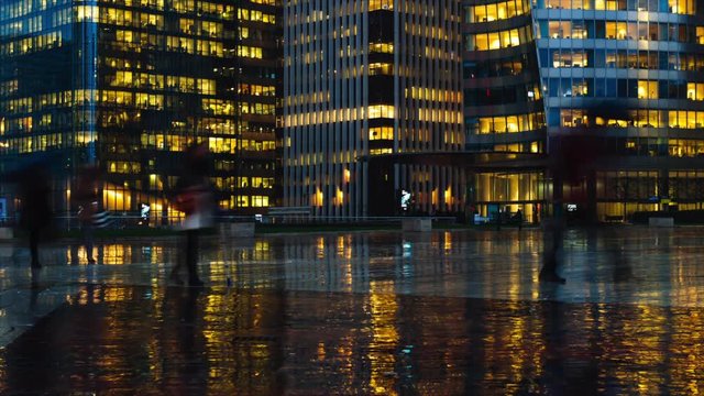 Time lapse of crowd of people walking near modern buildings in Paris business district La Defense. Night city lights, illuminated windows of office center. Concept of big city, business, job, economy