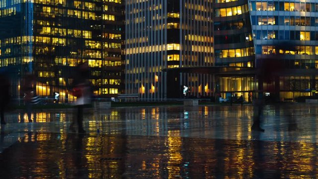Time lapse of crowd of people walking near modern buildings in Paris business district La Defense. Night city lights, illuminated windows of office center. Concept of big city, business, job, economy