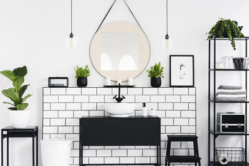 Mirror and poster above black washbasin in bathroom interior with plants and lamps. Real photo