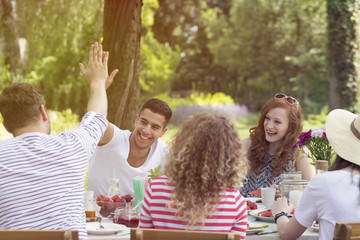 Two friends high-fiving each other and their girlfriends laughing during a garden party in the summer