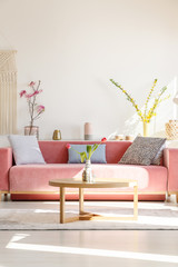 Cushions on red settee and wooden table in living room interior with flowers. Real photo