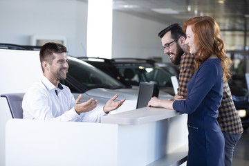 Smiling car seller talking with happy buyers in exclusive showroom