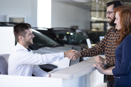 Car dealer and buyer shaking hands after transaction in luxury dealing salon