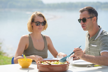 couple eating meal outdoors water in background