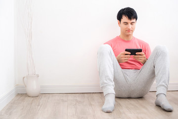 Handsome man sitting on the bedroom floor and playing game on his mobile phone in the morning  