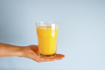 Hand holding glass of orange juice black straw isolated on blue background