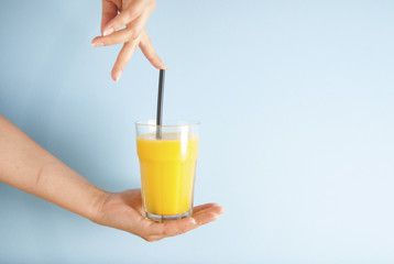 Hand holding glass of orange juice black straw isolated on blue background