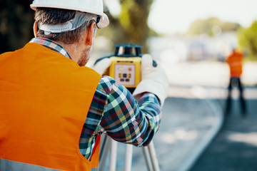 Geodesist in orange vest measuring with a total station - obrazy, fototapety, plakaty