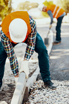 Builder in a hardhat and vest making a curb on the roadworks