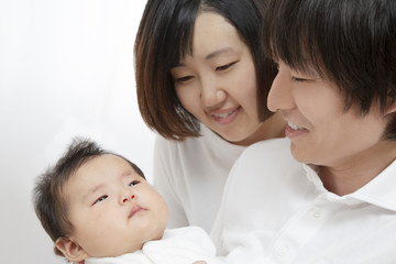 新生児を抱き見つめる若い夫婦、幸せな家族イメージ