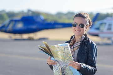 portrait of female pilot holding map helicopter in background