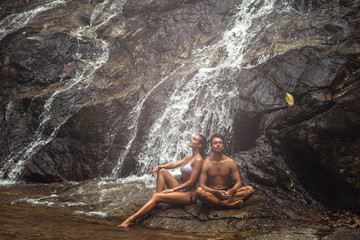 Couple is sitting  under the cold waterfall during hot day