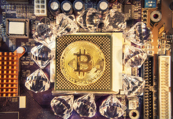 A golden physical bitcoin (digital virtual crypto-currency) placed over the CPU socket of a motherboard, surrounded by shiny diamonds.
