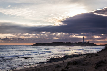 Great panorama of group of surfers enjoying waves on stunning sunset with Trafalgar lighthouse in...