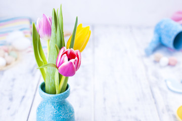 A bouquet of spring tulips of pink and yellow in a vase on the table. White background. Free space for text or a postcard. Easter